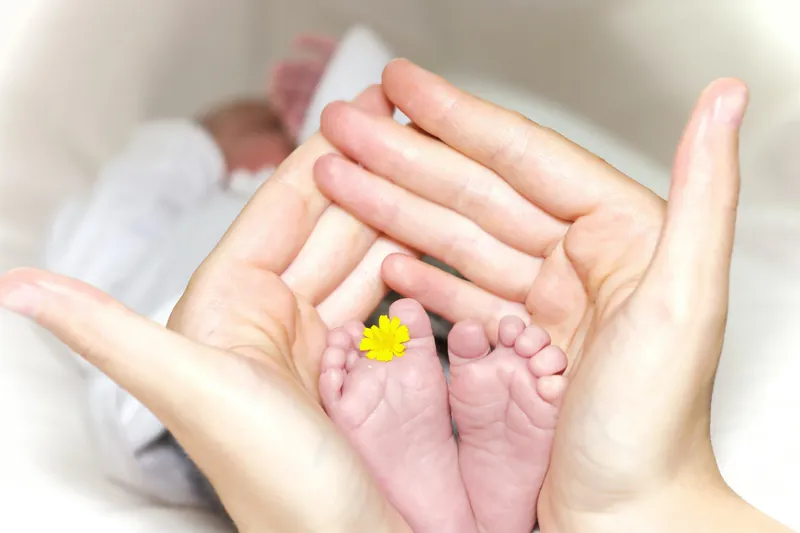 Twee handen vormen een kommetje rond babyvoetjes met een geel bloemetje