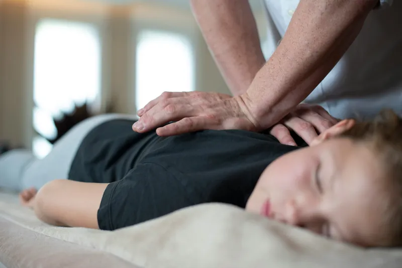 Kind ligt ontspannen op de massagetafel en krijgt een rugmassage